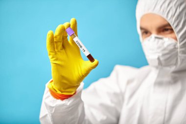 Solunum maskesi ve koruyucu tulum giyen laboratuvar teknisyeni Coronavirus 'un test ekspresi için tıbbi tüpü tutuyor..