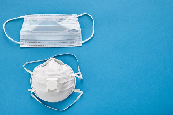 Coronavirus prevention disposable surgical masks and medical respirator on blue isolated, top view.