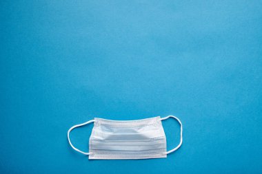 Mavi arka planda tıbbi maskenin yakın plan görüntüsü, boş alan, üst görüş. Karşılıklı tıbbi yardım ve destek kavramı.