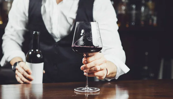 Sommelier sostiene una copa de vino tinto en el bar, de cerca . — Foto de Stock