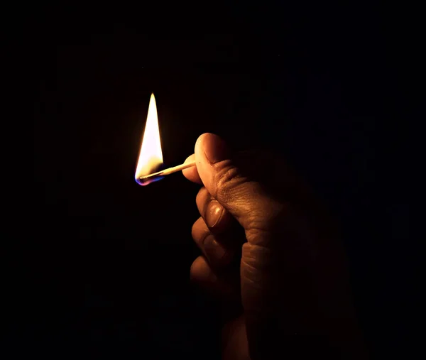A burning match in his hand. Hand with a burning match in the dark. Close up.