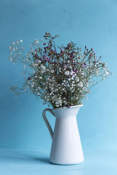 White vase with little flowers oon ligth blue background.