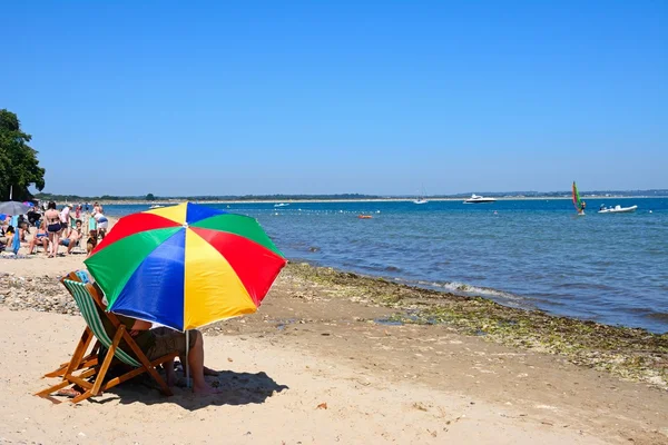 Nyaralók pihentető a strandon, az előtérben, a Studland Bay színes napernyővel. — Stock Fotó