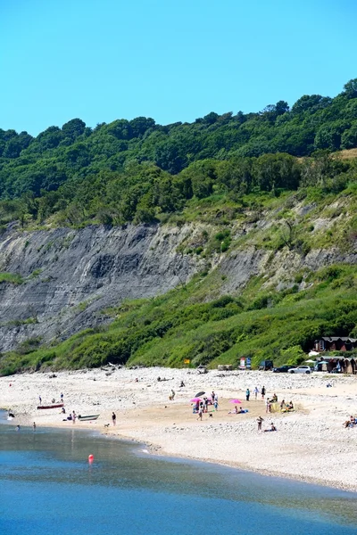 Отдыхающие отдыхают на пляже с гористыми скалами в задней части, Лайма Реджис . — стоковое фото