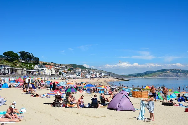 Les vacanciers se détendre sur la plage de sable avec la promenade et les cabanes de plage à l'arrière, Lyme Regis . — Photo