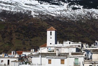 View over the town rooftops towards the church and snow capped mountains of the Sierra Nevada, Capileira, Spain. clipart