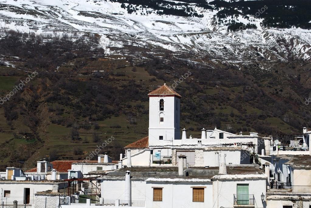 View over the town rooftops towards the church and snow capped mountains of the Sierra Nevada, Capileira, Spain.