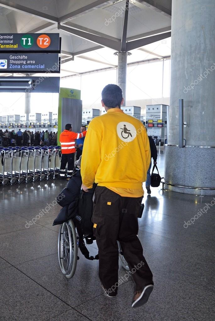 MALAGA, SPAIN - JANUARY 29, 2012 - Porter pushing passenger in wheelchair towards check-in desks in Terminal 3, Malaga airport, Malaga, Malaga Province, Costa del Sol, Andalucia, Spain, Western Europe, January 29, 2012.