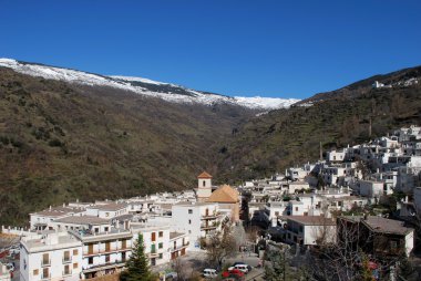 View across white village towards the snow capped mountains of the Sierra Nevada, Pampaneira, Spain. clipart