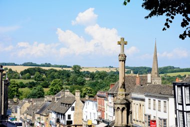 Dükkanlar ve işyerleri The Hill alışveriş caddesi ön planda, Burford, İngiltere Savaş Anıtı ile birlikte görünümünü.