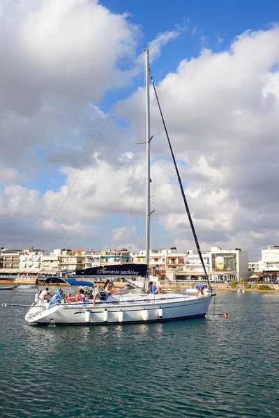 Turister avkopplande på en lyxig yacht i hamnen med restauranger vid vattnet till den bakre, Hersonissos, Kreta. — Stockfoto