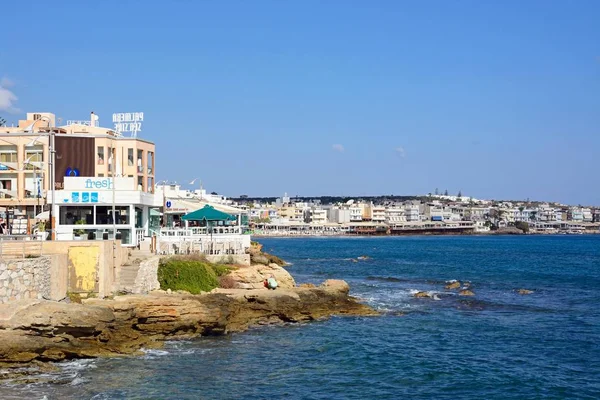 Vy över kusten kantas av restauranger med en stenig strand i förgrunden, Hersonissos, Kreta. — Stockfoto