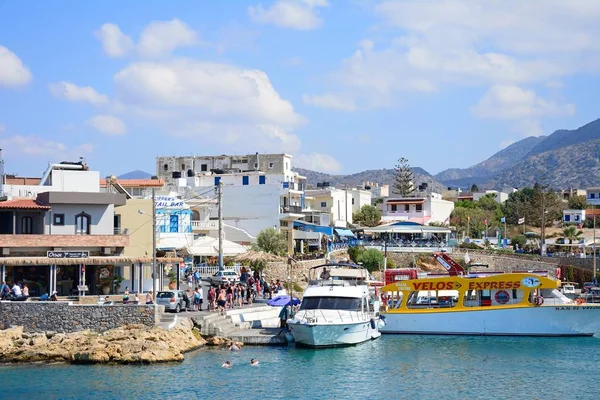 Boten aangemeerd in de haven met waterkant restaurants aan de achterzijde en toeristen genieten van de instelling, Sissi, Kreta. — Stockfoto