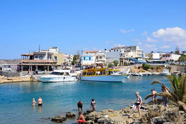 Touristes sur le rivage rocheux avec vue sur les bateaux et les restaurants à l'arrière, Sissi, Crète . — Photo