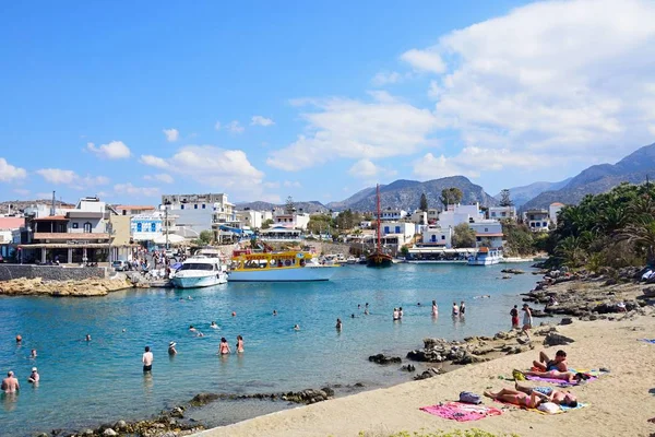 Toeristen in de zee en op het strand met uitzicht op de haven en stad, Sissi, Kreta. — Stockfoto