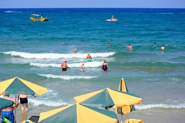 Turistas relajándose en el mar con sombrillas en primer plano, Stalida, Creta . — Foto de Stock