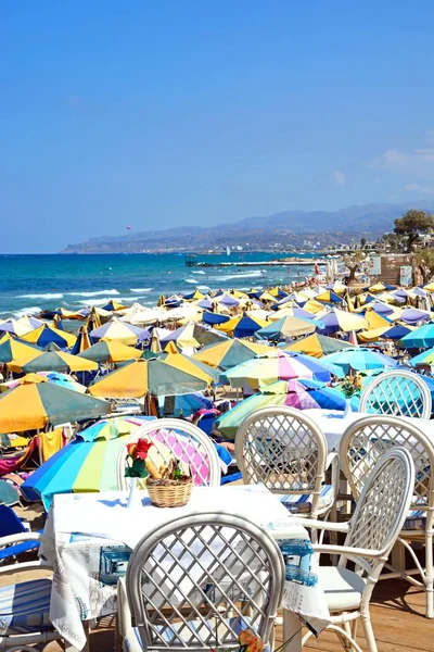 Turistas relaxando na praia com mesas de restaurante em primeiro plano e vistas para o mar, Stalida, Creta . — Fotografia de Stock