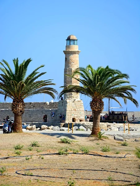 Keretes pálmafák a turisták mentén a kikötő fal, Rethymno, Kréta világítótornya. — Stock Fotó