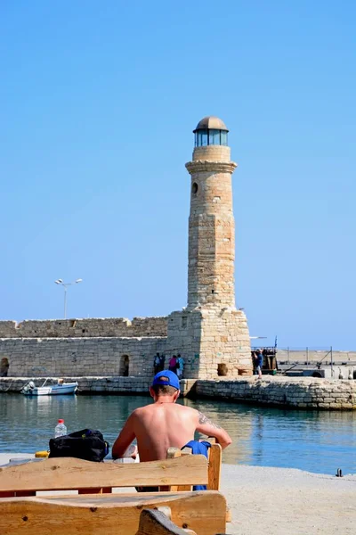 Перегляд маяка в гавані з людини, що сидить на лавці, на передньому плані, Ретімно, Крит. — стокове фото