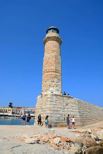 Utsikt över fyren i hamnen med turister promenader längs den seawall, Rethymno, Kreta. — Stockfoto