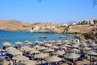 Ege Denizi ve kayalık kıyı şeridine bakan kumlu plajda rahatlatıcı turistler, Panormos, Girit, Yunanistan.