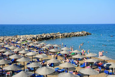 Kumsal ve deniz manzarası ile kumlu plajda rahatlatıcı turistler, Panormos, Girit, Yunanistan.