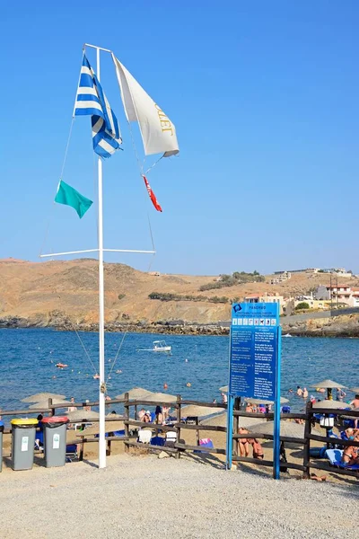 Kayalık sahil şeridine bakan plajın kenarında Yunan bayrağı ve bilgi tahtası, Panormos, Girit. — Stok fotoğraf