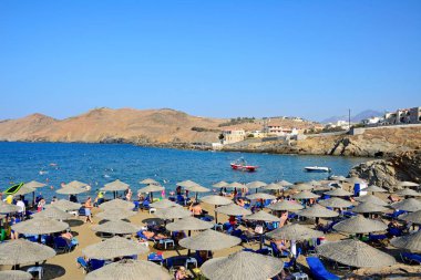 Ege Denizi ve kayalık sahil şeridi, Panormos, Crete doğru manzaralı kum plajındaki rahatlatıcı turist.