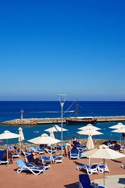 Turystów relaksujący na Hotel Mirabello słońce taras z portu z tyłu, Agios Nikolaos, Crete. — Zdjęcie stockowe