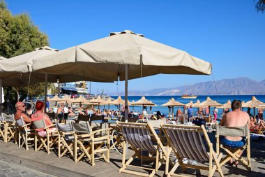 Turistler ön planda, Agios Nikolaos, Crete beachside restoranları ile sahilde rahatlatıcı.