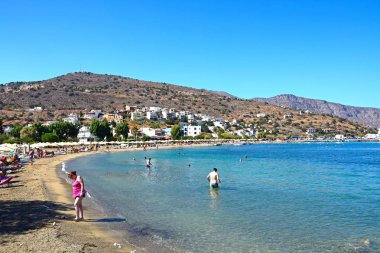 Turistler güneş ışığı, Elounda, Girit'te rahatlatıcı ile plaj ve kıyı şeridi görüntülemek.