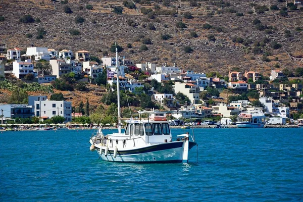 Kleine jacht afgemeerd in de baai met gebouwen aan de kust aan de achterzijde, Elounda, Crete. — Stockfoto