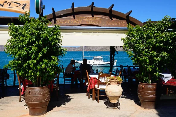 Paar sitzt an einem Tisch in der Taverne olondi entlang der Uferpromenade mit Blick auf die Bucht, elounda, Beton. — Stockfoto