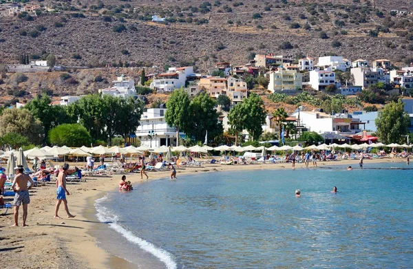 Turistler güneş ışığı, Elounda, Girit'te rahatlatıcı ile plaj ve kıyı şeridi görüntülemek.