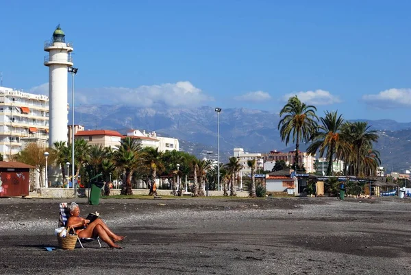 Femme bronzant sur la plage lisant un livre avec vue sur le phare, Torre del Mar, Espagne . — Photo