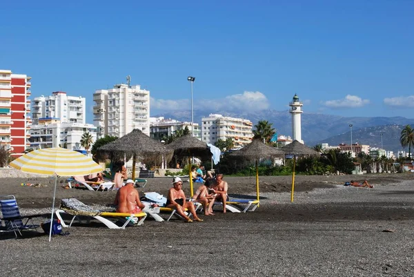 Τουρίστες ηλιοθεραπεία στην παραλία με θέα προς τον φάρο, το Torre del Mar, Ισπανία. — Φωτογραφία Αρχείου