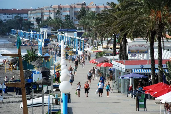 Turister promenader längs strandpromenaden med uteserveringar till höger hand sida och stranden till vänster, Torrox Costa, Spanien. — Stockfoto