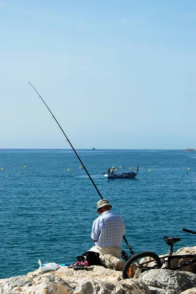 Hombre pescando desde el rompeolas con vistas al mar, Torremolinos, España . — Foto de Stock