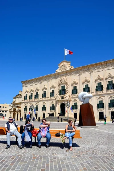 Pohled Auberge de Castille Castille náměstí s Bianco Carrara mramorové sochy a turisty sedí na lavičce v popředí, Valletta, Malta. — Stock fotografie