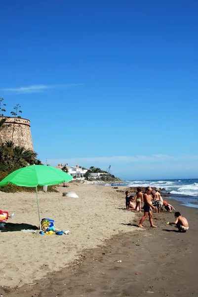 Turistas relajándose en la playa de Playa de las Canas con la antigua atalaya en la parte trasera, Marbessa, Marbella . —  Fotos de Stock