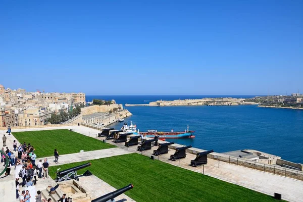 Soldados preparando los cañones listos para el cañón del mediodía en los Jardines del Alto Barrakka con vistas a través del Gran Puerto hacia Fort Rikasoli y los turistas mirando en, La Valeta, Malta . — Foto de Stock