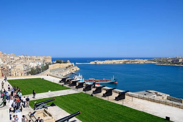 Soldater förbereder kanoner redo för Noon pistolen i Upper Barrakka Gardens med utsikt över Grand Harbour mot Fort Rikasoli och turister titta på, Valletta, Malta. — Stockfoto