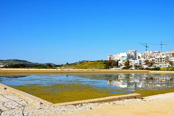 Utsikt över saltdammar med byggnader och byggkranar bakåt i Salina Bay, Buġibba, Malta. — Stockfoto