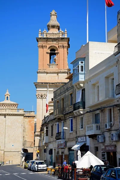Kijk langs de waterkant winkels naar St Lawrence kerktoren, Vittoriosa, Malta. — Stockfoto