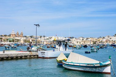 Geleneksel Malta Dghajsa balıkçı tekneleri ve liman waterfront binaları ile arka, Marsaxlokk, Malta.