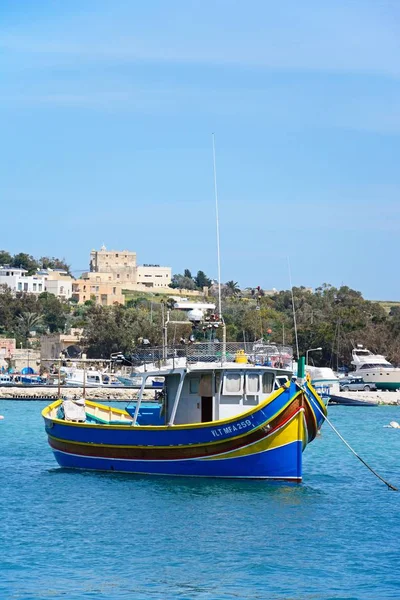 Традиционные мальтийские Dghajsa рыбацкая лодка в гавани с прибрежными зданиями в задней части, Марсашлок, Мальта . — стоковое фото