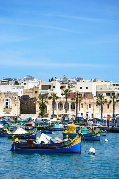 Barcos de pesca tradicionais malteses Dghajsa no porto com edifícios à beira-mar na parte traseira, Marsaxlokk, Malta . — Fotografia de Stock