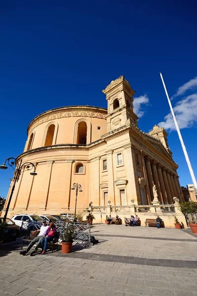 Mosta 的圆形大厅的景观与游客坐在前台的长椅上, Mosta, 马耳他. — 图库照片