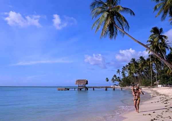 Man lopen langs het strand met een kind met uitzicht op de steiger op Pigeon Point, Tobago. — Stockfoto