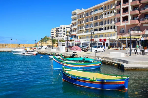 Традиционные мальтийские рыбацкие лодки Dghajsa в гавани с барами и ресторанами в задней части, Марсалфорн, Гозо, Мальта, Европа . — стоковое фото